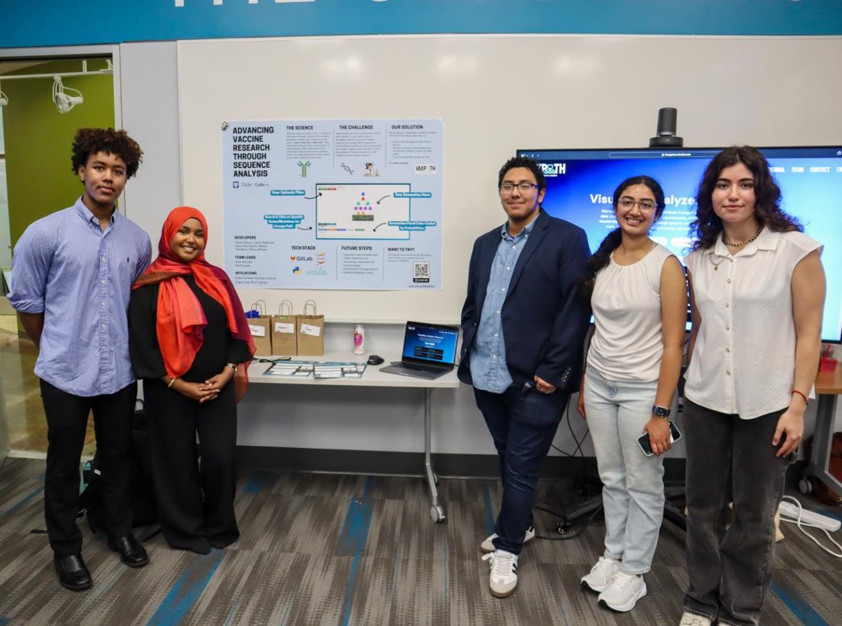 A group of five Code+ 2025 students stand in front of their project poster and a monitor at the +Programs Poster Session.